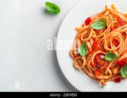 Linguini Pasta mit Tomatensauce und Basilikum auf grauem Hintergrund. Stockfoto
