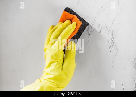 Weibliche Hand, die die schützenden Rübenhandschuhe trägt, löscht die Kinderzeichnungen von der schmutzigen Wand Stockfoto