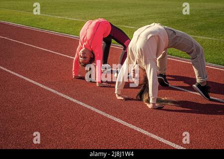 Flexible Mädchen Turnerinnen stehen in Krabbenposition auf der Leichtathletik-Strecke, Flexibilität Stockfoto