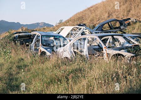 Schrottplatz, Autodumpe, Metallschrott. Ein Haufen beschädigter, zerbrochener, rostiger Autos wuchs mit Gras in der Nähe des größten Sees des kaukasus, Sevan, in den Vororten von Stockfoto