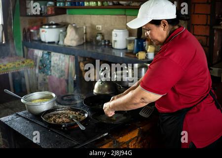 Frau, die sich auf das Kochen in ihrem kleinen costaricanischen typischen Lebensmittelgeschäft konzentriert. Stockfoto