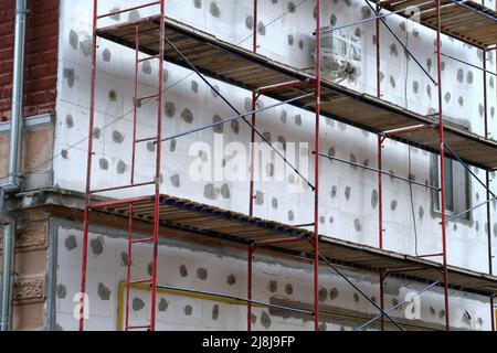 Die Gebäudefassade wird gerade renoviert und der Gerüstrahmen ist im Bau. Wandisolierung mit Styroporplatten für energieeffizientes Zuhause Stockfoto