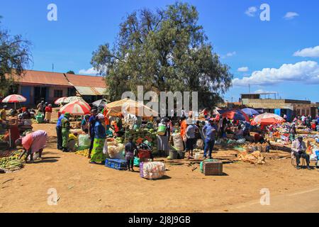 Vielbeschäftigter Markt am Straßenrand mit Menschen, die Obst und Gemüse verkaufen. Bunte Sonnenschirme an Marktständen. Dorfstraße, Kenia, Afrika Stockfoto