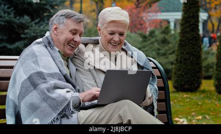 Ältere glücklich kaukasischen Ehemann Frau ältere ältere ältere Paar Großeltern Familie Blick auf Bildschirm Laptop Arbeit Remote Browser gute Nachrichten sehen lustige Video Stockfoto