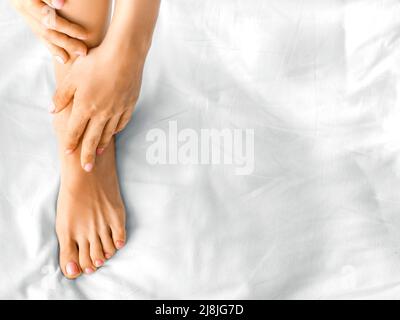 Frauenfuß auf einem weißen Laken. Sie massiert ihren Fuß oder trägt Feuchtigkeitscreme auf. Nahaufnahme. Stockfoto