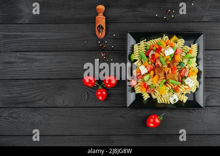 Penne-Pasta mit Gemüse, Erbsen, Paprika, Tomaten, Sauce, Mozzarella-Käse auf schwarzem Holzboden. Italienische Pasta mit Gemüse und sp Stockfoto