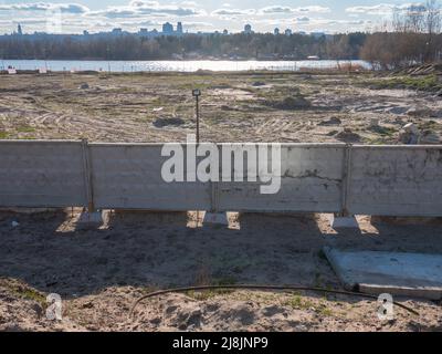 Der Panoramablick über die Baustelle hinter dem Betonzaun am Ufer des Flusses Dnipro und das rechte Ufer von Kiew am Horizont. Stockfoto