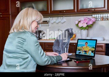 Reife Geschäftsfrau, die auf einer Videokonferenz mit einem Kollegen zu Hause in der Küche spricht Stockfoto