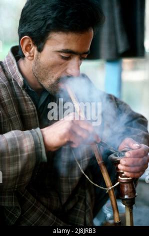 Mann raucht Wasserleitung in Srinagar, Kaschmir 1986 Stockfoto