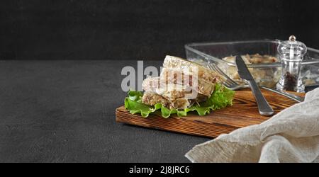 Fleisch Aspik, Gelees langsam gekochtes Fleisch lag in Stücken auf einem Blatt Salat auf einem dunklen Hintergrund Stockfoto