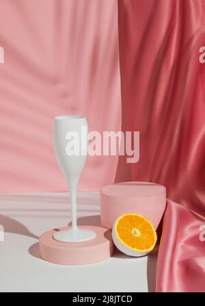 Weinglas mit frischen orangen Früchten, tropischem Palmenblatt-Schatten und Podium auf pastellrosa Hintergrund. Sommergetränk Minimales Konzept. Geeignet für Produkt Stockfoto