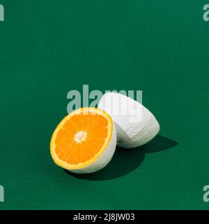 Weiß bemaltes orangefarbenes Obst, halbiert auf grünem Hintergrund. Minimales Lebensmittelkonzept. Speicherplatz kopieren. Stockfoto