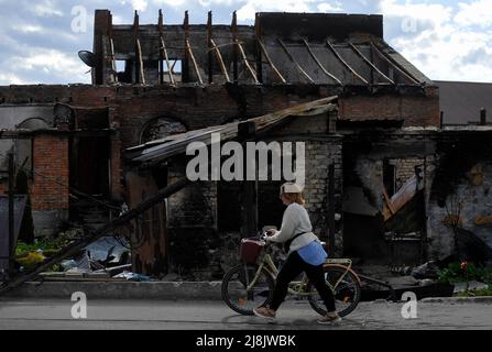 Irpin, Ukraine. 16.. Mai 2022. Eine Frau kommt an einem zerstörten Haus vorbei, das durch den Beschuss der russischen Armee in der Stadt Irpin in der Nähe der ukrainischen Hauptstadt Kiew beschädigt wurde. Russland marschierte am 24. Februar 2022 in die Ukraine ein und löste damit den größten militärischen Angriff in Europa seit dem Zweiten Weltkrieg aus (Foto: Sergei Chuzavkov/SOPA Images/Sipa USA) Quelle: SIPA USA/Alamy Live News Stockfoto