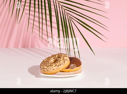 Tropisches Palmblatt und Donuts mit Schokolade auf pastellrosa Hintergrund gekrönt. Minimales Lebensmittelkonzept. Stockfoto