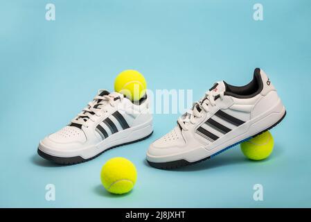 Belgrad, Serbien - 11. Mai 2022. Neue Adidas Tennisschuhe auf blauem Hintergrund mit Tennisbällen. Neue Adidas Sneakers oder Sportschuhe auf blauem Hintergrund. Männer Stockfoto