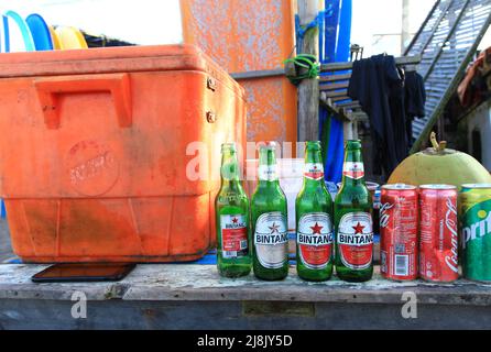 Eine Strandbar in Canggu, Bali, Indonesien, mit einer orangefarbenen Kühlbox und mehreren Leergut, darunter einheimische Biere Bintang, Coca Cola und Sprite Dosen. Stockfoto