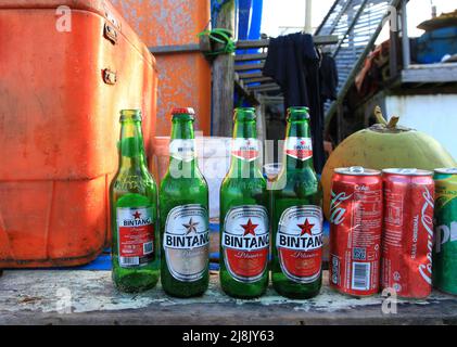 Eine Strandbar in Canggu, Bali, Indonesien, mit einer orangefarbenen Kühlbox und mehreren Leergut, darunter einheimische Biere Bintang, Coca Cola und Sprite Dosen. Stockfoto