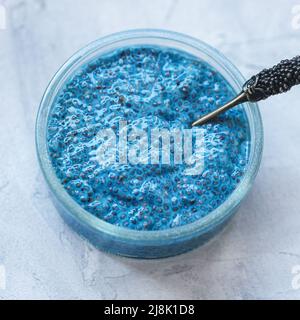 Blaue Chia-Samenpudding-Schüssel mit Löffel. Superfood und veganes Lebensmittelkonzept. Grauer Hintergrund, Kopierbereich. Nahaufnahme, Draufsicht Stockfoto