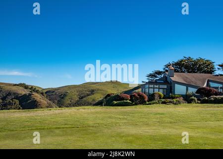 Grüne Hügel umgeben ein sehr geometrisches Haus unter einem großen blauen Himmel. Entlang der Golfplatz Gemeinschaft in Bodega Bay, CA. Stockfoto