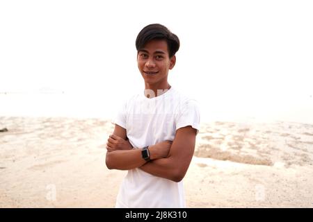 Asiatischer junger Mann mit gekreuzten Armen und digitalem Bazelet am Strand Stockfoto