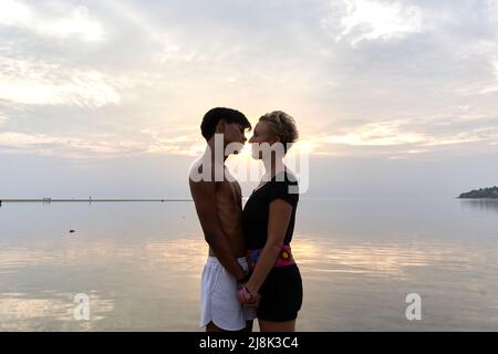 Nahaufnahme der Silhouette eines Paares, das sich bei Sonnenuntergang ins Meer küsst Stockfoto
