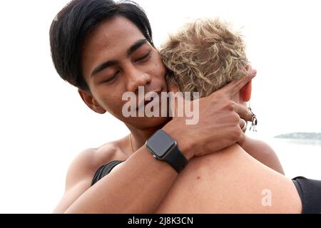 Ein junger asiatischer Mann umarmt eine Erwachsene kaukasische Frau am Meer Stockfoto