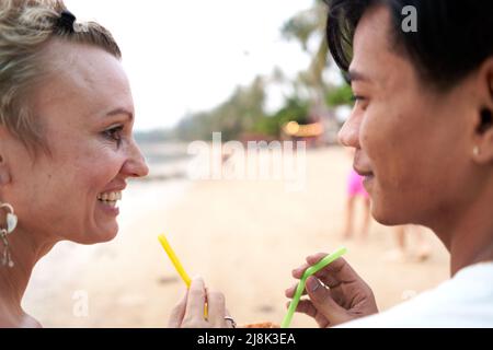 Liebhaber, die sich gegenseitig zuschauen, während sie am Strand einen Kokosnusssaft teilen Stockfoto