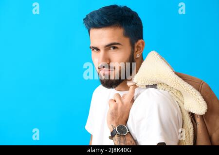 Stilvoller bärtiger junger Mann mit ungewöhnlichen Haaren und Tattoo auf blauem Hintergrund Stockfoto