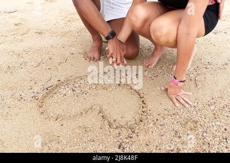 Detail einer Herzform im Sand eines Strandes neben einem Paar Stockfoto