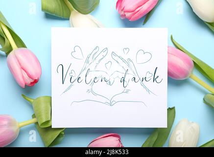 Karte mit Text VIELEN DANK und Tulpenblumen auf hellblauem Hintergrund Stockfoto