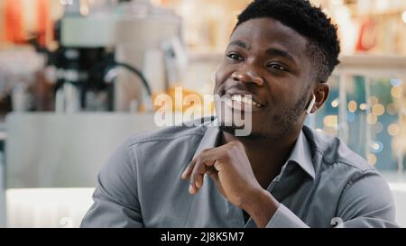 Nahaufnahme junger, glücklicher afroamerikanischer Mann, der über kabellose Kopfhörer spricht und lächelt und freundlich auf einen geschäftlichen Anruf reagiert und erklärt Stockfoto