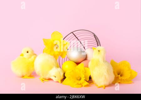 Niedliche gelbe Hühner, umgedrehten Korb mit Ostereiern und Blumen auf rosa Hintergrund Stockfoto