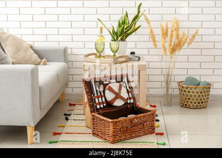 Korbkorb mit Geschirr für Picknick auf Teppich im Wohnzimmer Stockfoto