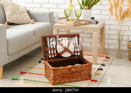 Korbkorb mit Geschirr für Picknick auf Teppich im Wohnzimmer Stockfoto