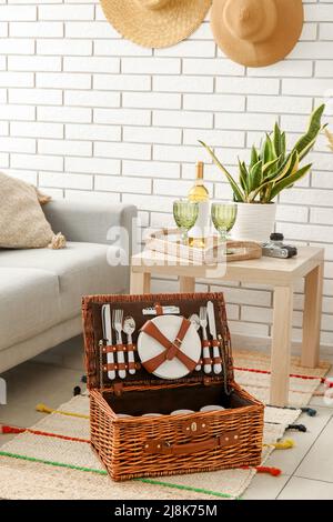 Korbkorb mit Geschirr für Picknick auf Teppich im Wohnzimmer Stockfoto