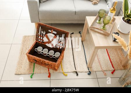 Korbkorb mit Geschirr für Picknick auf Teppich im Wohnzimmer Stockfoto