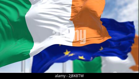 Detail der im Wind winkenden Nationalflagge Irlands mit verschwommener Flagge der europäischen Union. Im Hintergrund an einem klaren Tag. Demokratie und Politik. Stockfoto