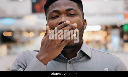 Männliches Porträt Nahaufnahme Mann überarbeiteter junger afroamerikanischer Mann müder Arbeiter, der auf die Kamera schaut Gähnen bedeckt den Mund mit der Hand gelangweilt fühlt sich müde schläfrig an Stockfoto