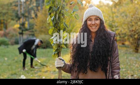 Nahaufnahme junge glücklich lächelnde Mädchen im Freien stehend halten Keimling in der Hand Mann graben Loch für die Pflanzung von Baum im Hintergrund Freiwillige Öko-Aktivisten Stockfoto
