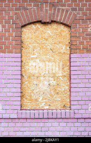 Ziegelfassade des Hauses mit einem Fenster, das mit Spanplatten blockiert ist Stockfoto
