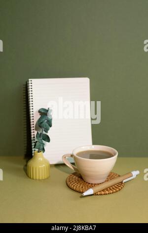 Notizbuch und Tasse Kaffee auf dem Schreibtisch. Khaki grüner Hintergrund Stockfoto