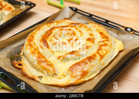 Türkischer nationaler Schneckenteig Kolberegi aus knusprigem Filoteig mit Spinat- und Suluguni-Füllung in saurer Rahm- und Eierkonfitüre Stockfoto