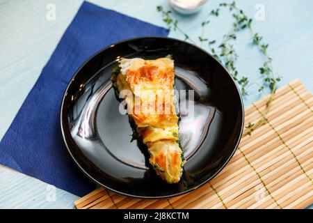 Türkischer nationaler Schneckenteig Kolberegi aus knusprigem Filoteig mit Spinat- und Suluguni-Füllung in saurer Rahm- und Eierkonfitüre Stockfoto