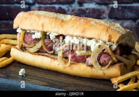 Nahaufnahme eines Steak-Sandwiches mit Zwiebeln und Blauschimmelkäse, serviert mit Pommes frites. Stockfoto