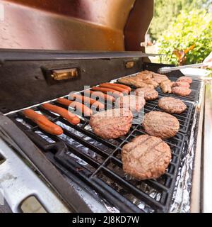 Grillen von Burger und Hunden auf einem Gasgrill an einem sonnigen Tag im Sommer Stockfoto