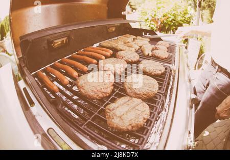 Verblasste Film-Aufnahme vom Grillen von Burgers and Dogs auf einem Gasgrill an einem sonnigen Tag im Sommer Stockfoto