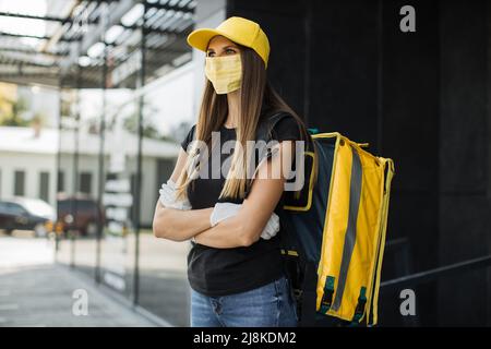Lieferung von Lebensmitteln, Porträt einer kaukasischen Frau mit Gesichtsschutzmaske, die während einer Pandemie der Covid-19 mit gelbem Rucksack arbeitete. Schneller Service, Arbeitskonzept für Ausländer, einfacher Beruf. Stockfoto