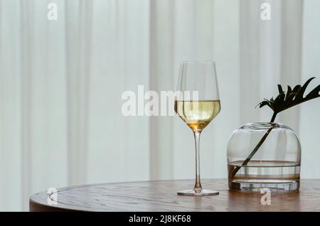 Eine Glasse Weißwein auf Holztisch mit Vorhang Hintergrund. Stockfoto