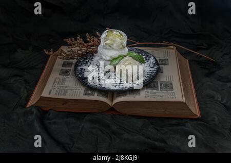 Grüner Tee und Daifuku mit roten Bohnen über altem Buch auf dunklem Hintergrund. Japanischer traditioneller Snack, Kopierraum, selektiver Fokus. Stockfoto