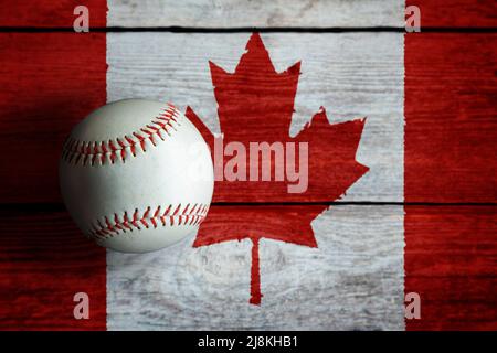 Leder-Baseballspiel auf rustikalem Holzhintergrund mit kanadischer Flagge mit Kopierraum bemalt. Kanada ist eine der führenden Baseballnationen der Welt. Stockfoto